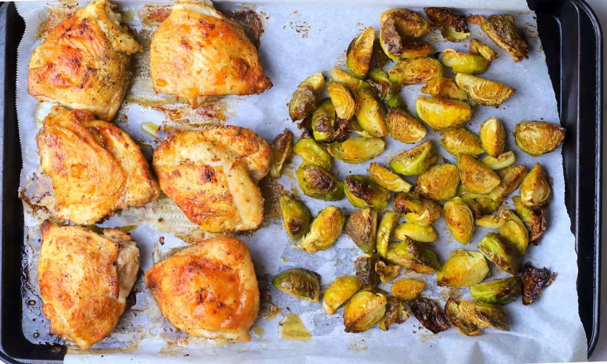 Low carb baked chicken thighs with roasted brussels sprouts on a parchment lined sheet pan.