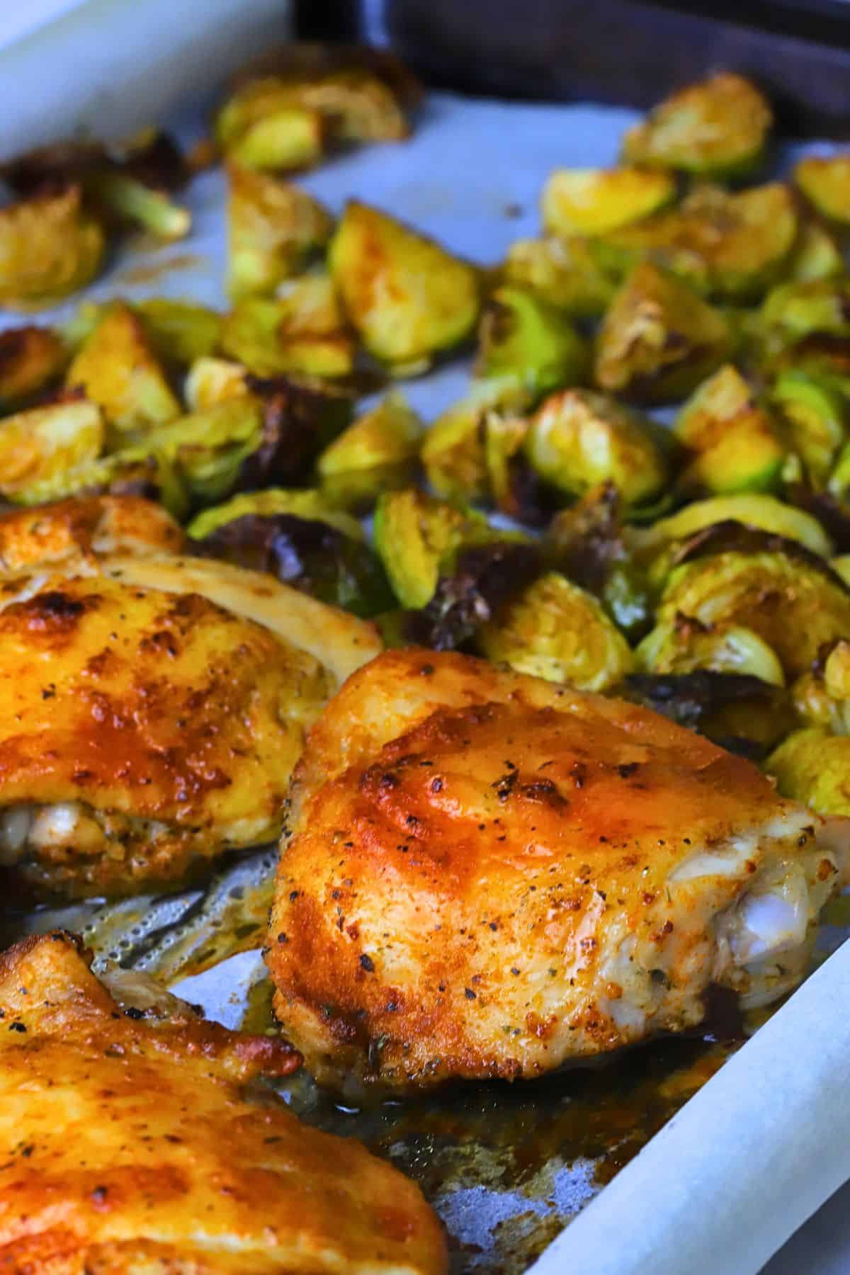 Low carb baked chicken thighs with roasted brussels sprouts on a parchment lined sheet pan.