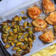 Low carb baked chicken thighs with roasted brussels sprouts on a parchment lined sheet pan.