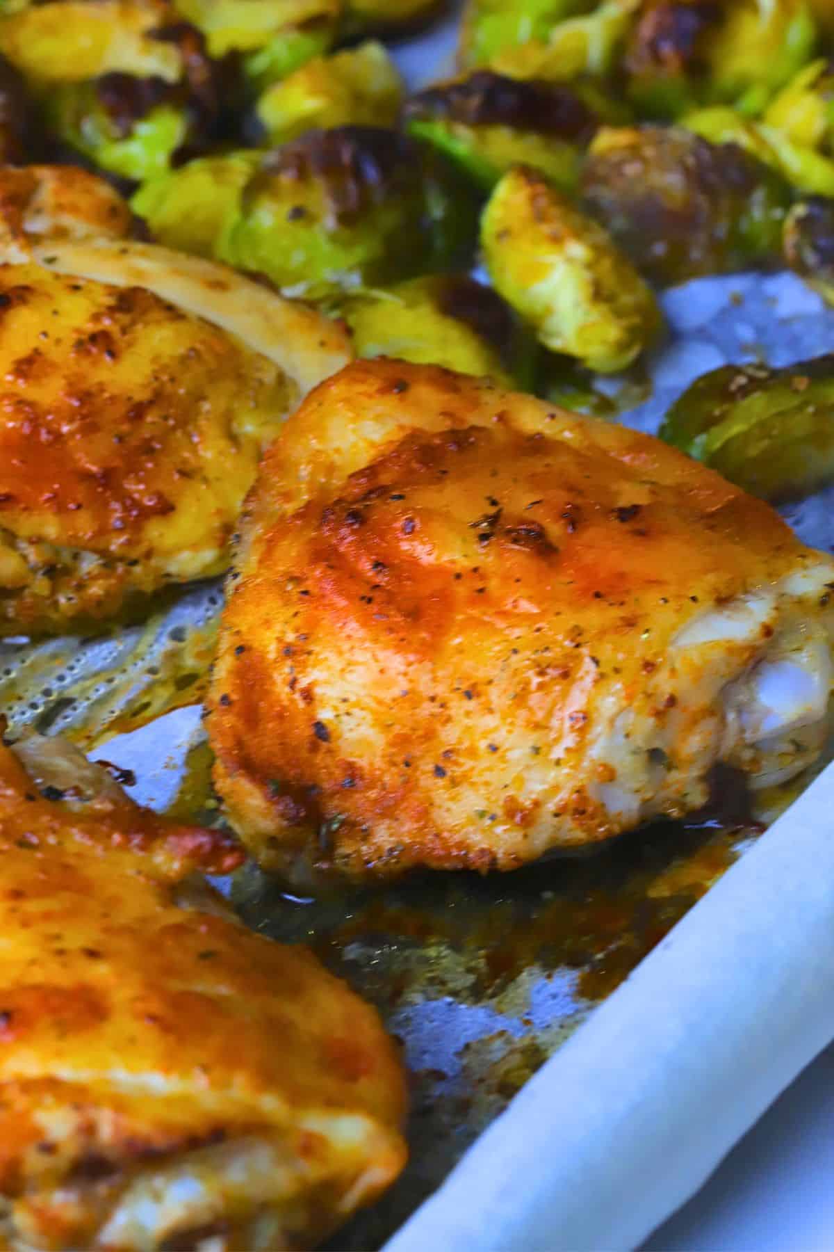 Close up of low carb baked chicken thighs with roasted brussels sprouts on a parchment lined sheet pan.