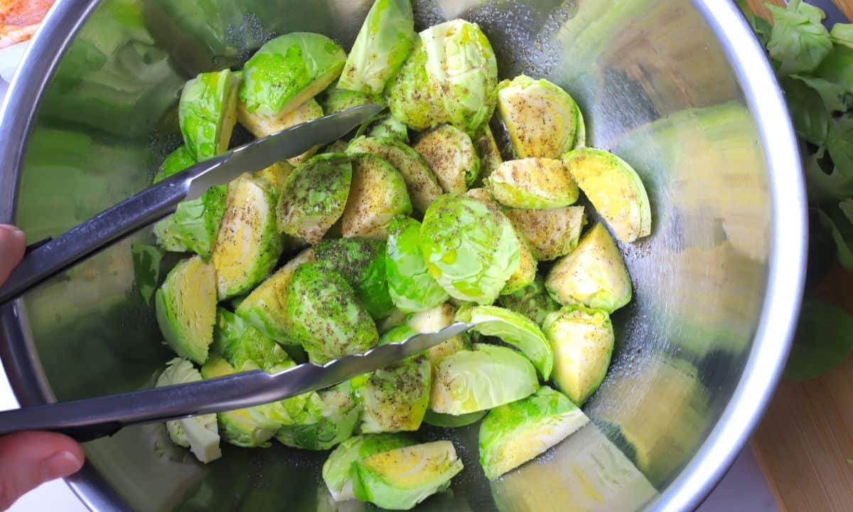 Tossing the brussels sprouts in a bowl with tongs.