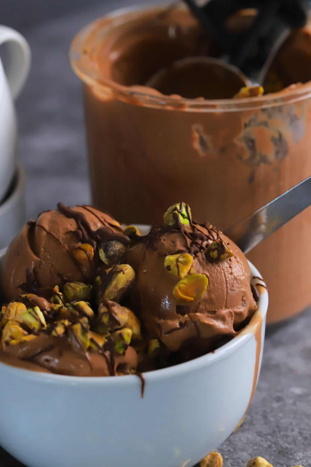 Dubai chocolate pistachio ice cream in a bowl next to the ninja creami pint with more ice cream.