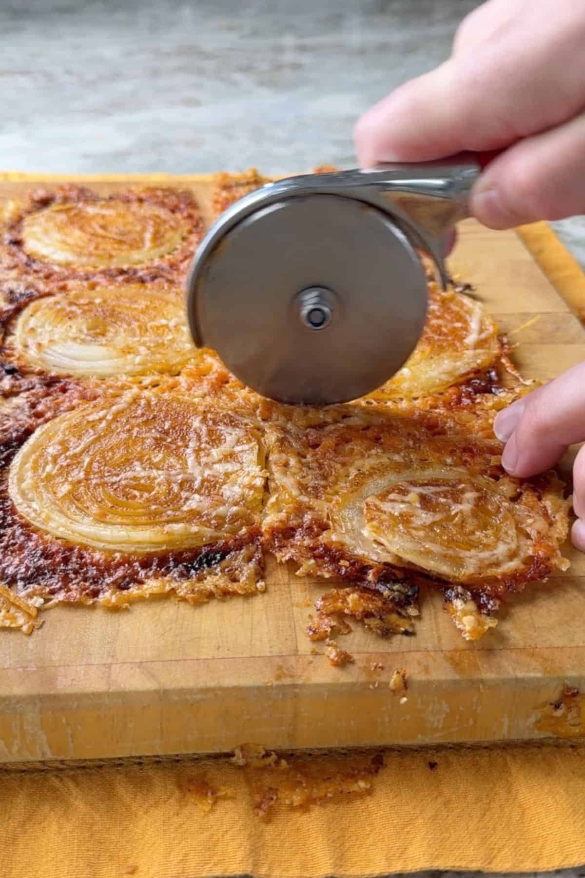 Cutting the 2 ingredient onion ring chips on a cutting board with a pizza knife.